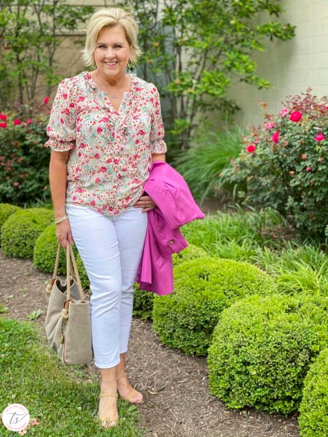 Fashion Blogger 50 Is Not Old is wearing a feminine floral blouse, white crop pants, cork heels, and a Michael Kors handbag