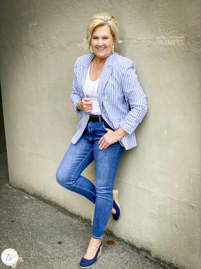 Fashion Blogger 50 Is Not Old is wearing a striped blazer, a white v-neck bodysuit, skinny jeans, and navy espadrilles