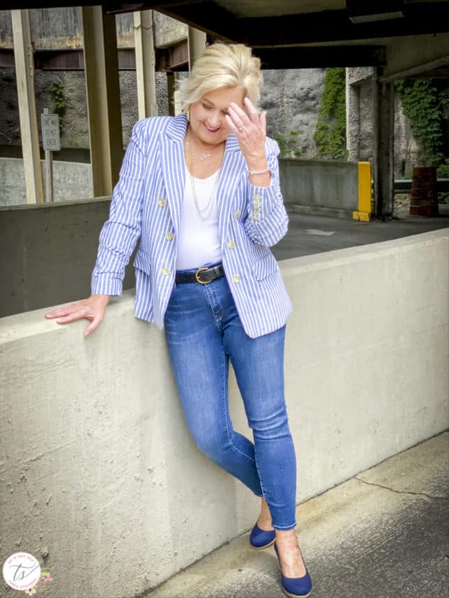 Fashion Blogger 50 Is Not Old is wearing a striped blue and white blazer, a white v-neck bodysuit, Mavi skinny jeans, and navy espadrilles