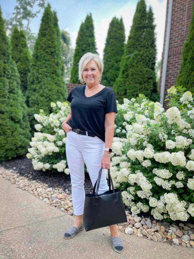 Fashion Blogger 50 Is Not Old is wearing a black v-neck t-shirt with white ankle pants, a black leather handbag, and Chanel espadrille shoes