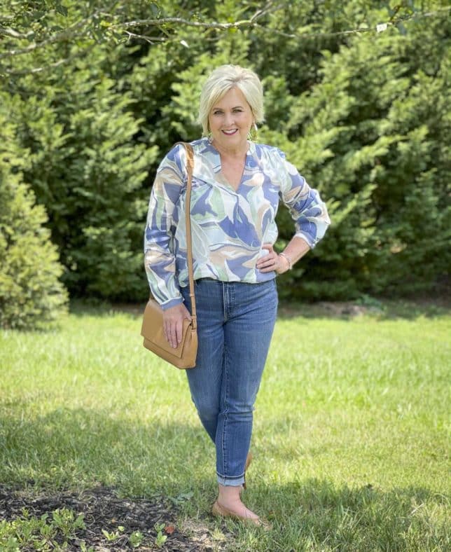 Fashion Blogger 50 Is Not Old is wearing a v-neck long sleeve top with cuffed jeans, a camel crossbody handbag, and flats by Tory Burch