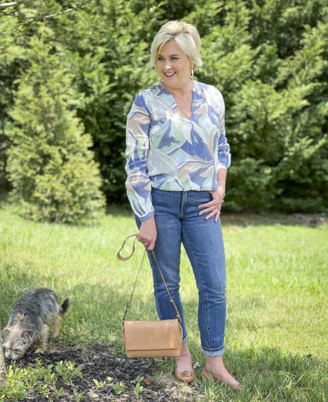 Fashion Blogger 50 Is Not Old is wearing a v-neck long sleeve top with cuffed jeans, and holding a camel crossbody handbag, flats by Tory Burch