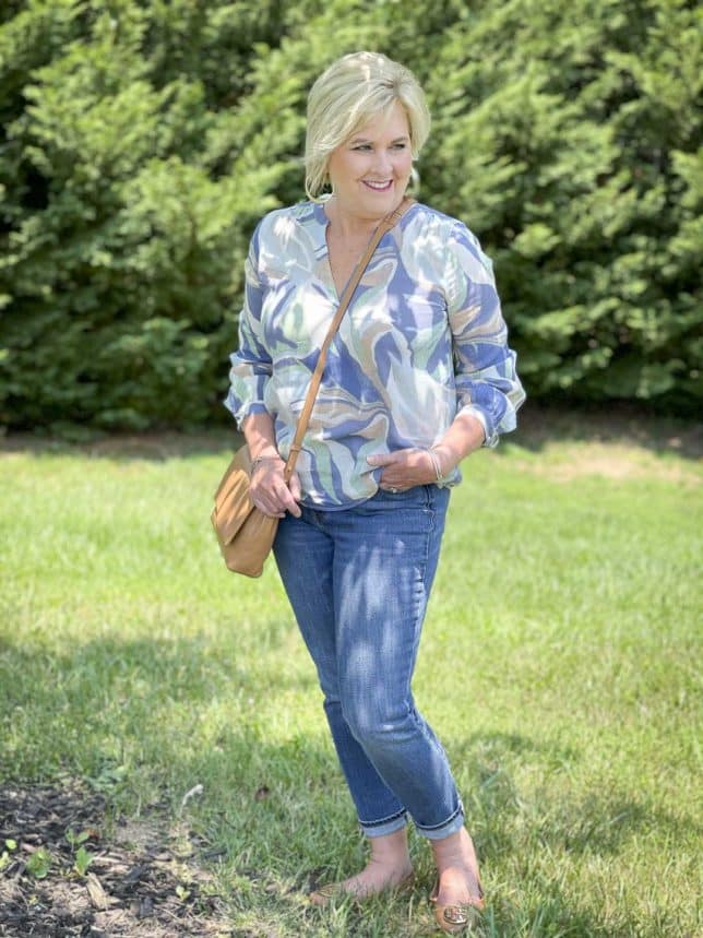 Fashion Blogger 50 Is Not Old is wearing a v-neck long sleeve top with cuffed jeans, a crossbody handbag, and flats by Tory Burch