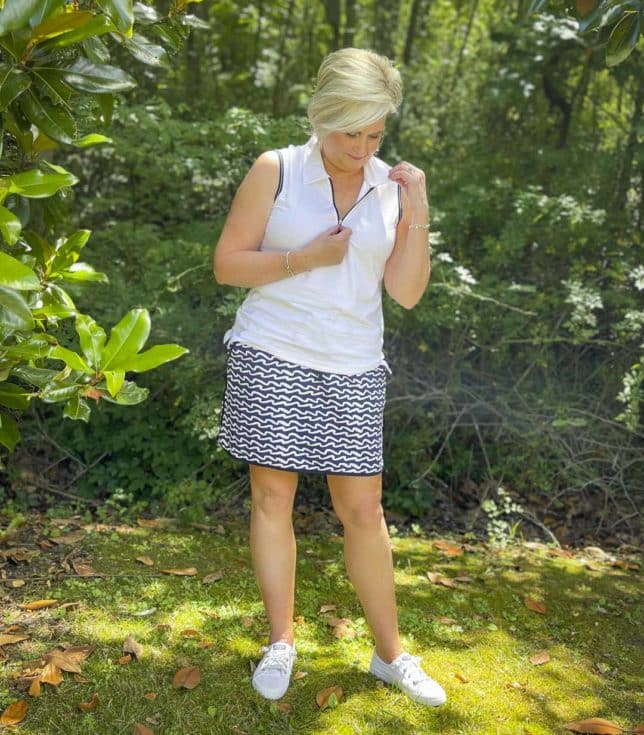 Fashion Blogger 50 Is Not Old is wearing a navy and white wave skort with a white quarter zip top with navy trim, and white Sperry sneakers