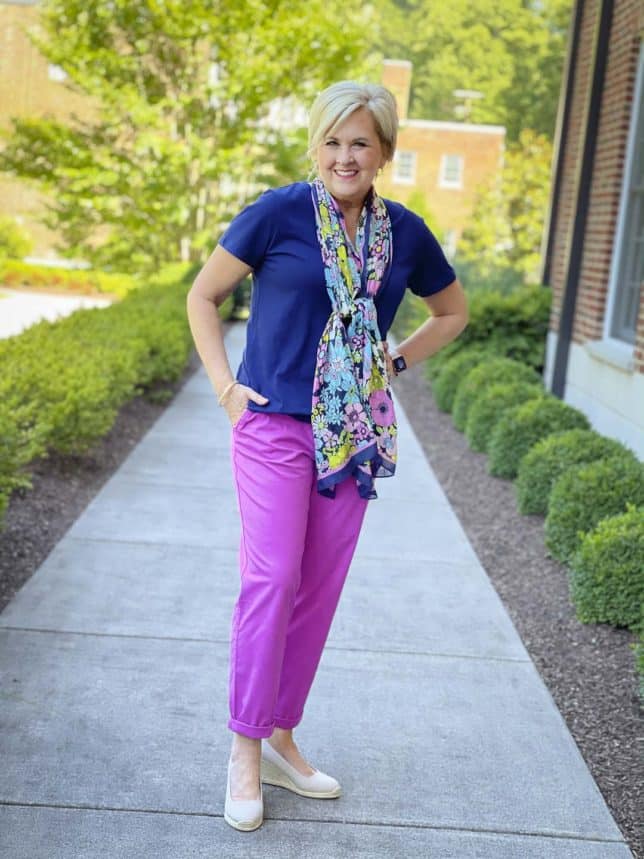 Fashion Blogger 50 Is Not Old is wearing a navy t-shirt with purple orchid chinos pants and a navy floral scarf around her neck