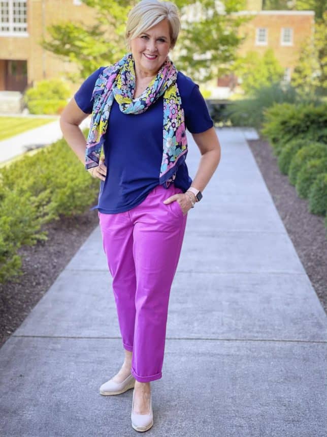 Fashion Blogger 50 Is Not Old is wearing a navy t-shirt with purple orchid chinos pants and has tied a floral scarf around her neck