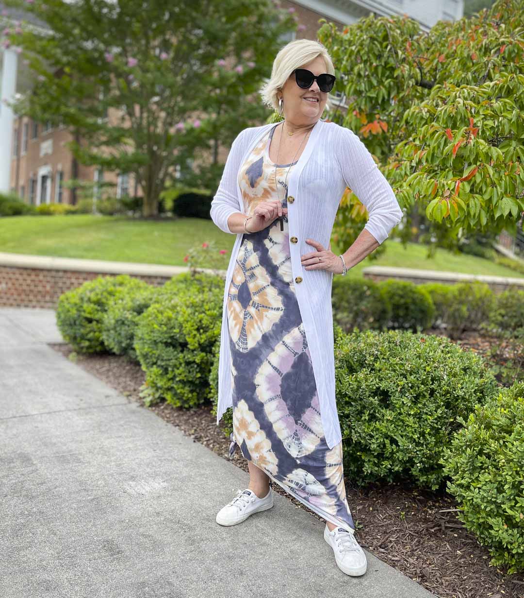 Fashion Blogger 50 Is Not Old is wearing a summery outfit consisting of a tie-dye maxi dress, a white duster and white Sperry sneakers