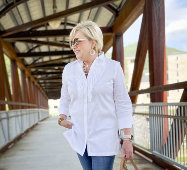 Over 40 Fashion Blogger, Tania Stephens, is standing on a bridge wearing a white button down shirt with a large ruffle
