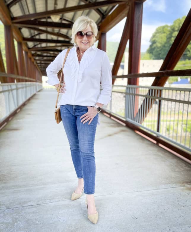 Over 40 Fashion Blogger, Tania Stephens, is on a bridge wearing a white button down shirt with a large ruffle, ankle length jeans, and neutral kitten heels