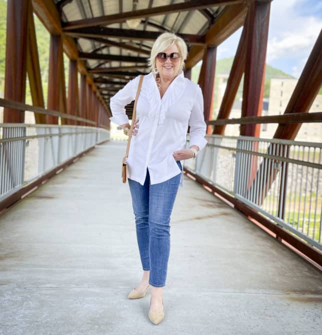 Over 40 Fashion Blogger, Tania Stephens, is wearing a white button down shirt with a large ruffle, ankle length jeans, and neutral kitten heels