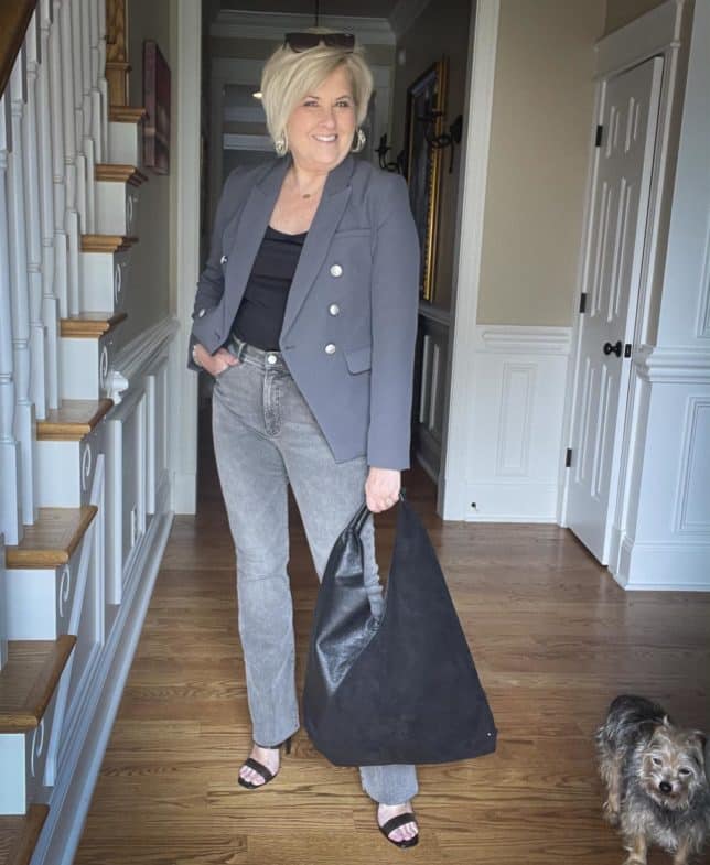 Over 40 Fashion Blogger, Tania Stephens, is styling a double-breasted gray blazer with a black bodysuit, gray raw hem jeans, black heels, and a large black handbag