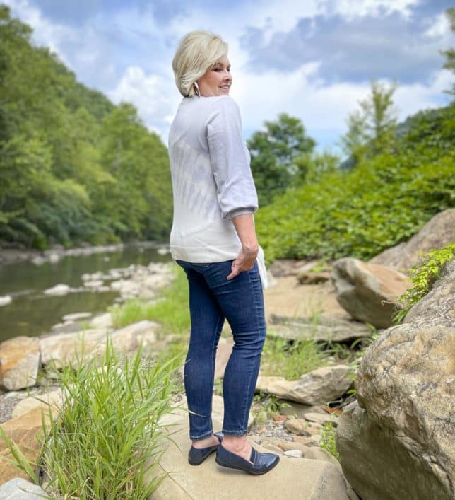 Over 40 Fashion Blogger, Tania Stephens is showing the back of a tie-dye side knot sweater, jeans, and navy loafers