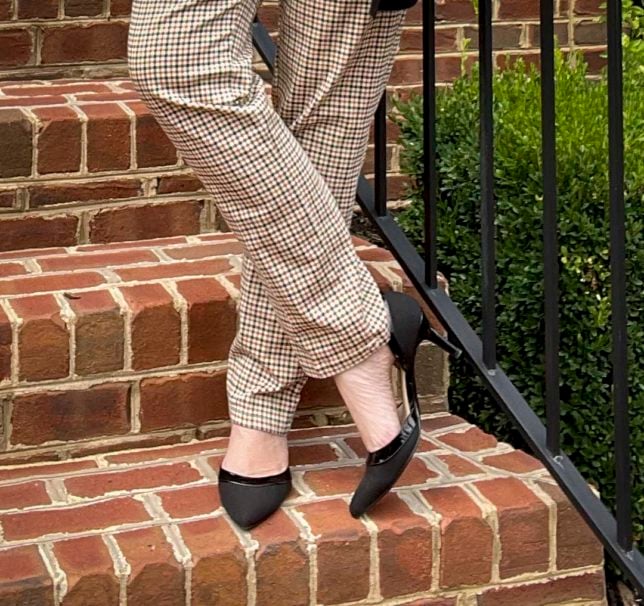 Fashion Blogger 50 Is Not Old is standing on steps wearing a pair of plaid pants and black heels
