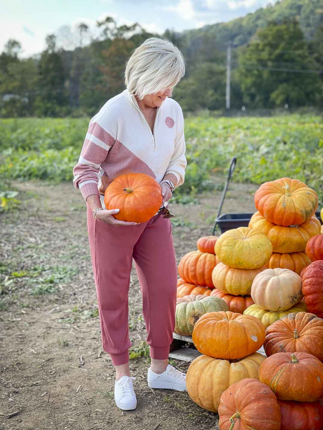 Over 40 Fashion Blogger, Tania Stephens is standing in a pumpkin patch in a Lou & Grey sweater, a pair of joggers, and picking our a pumpkin