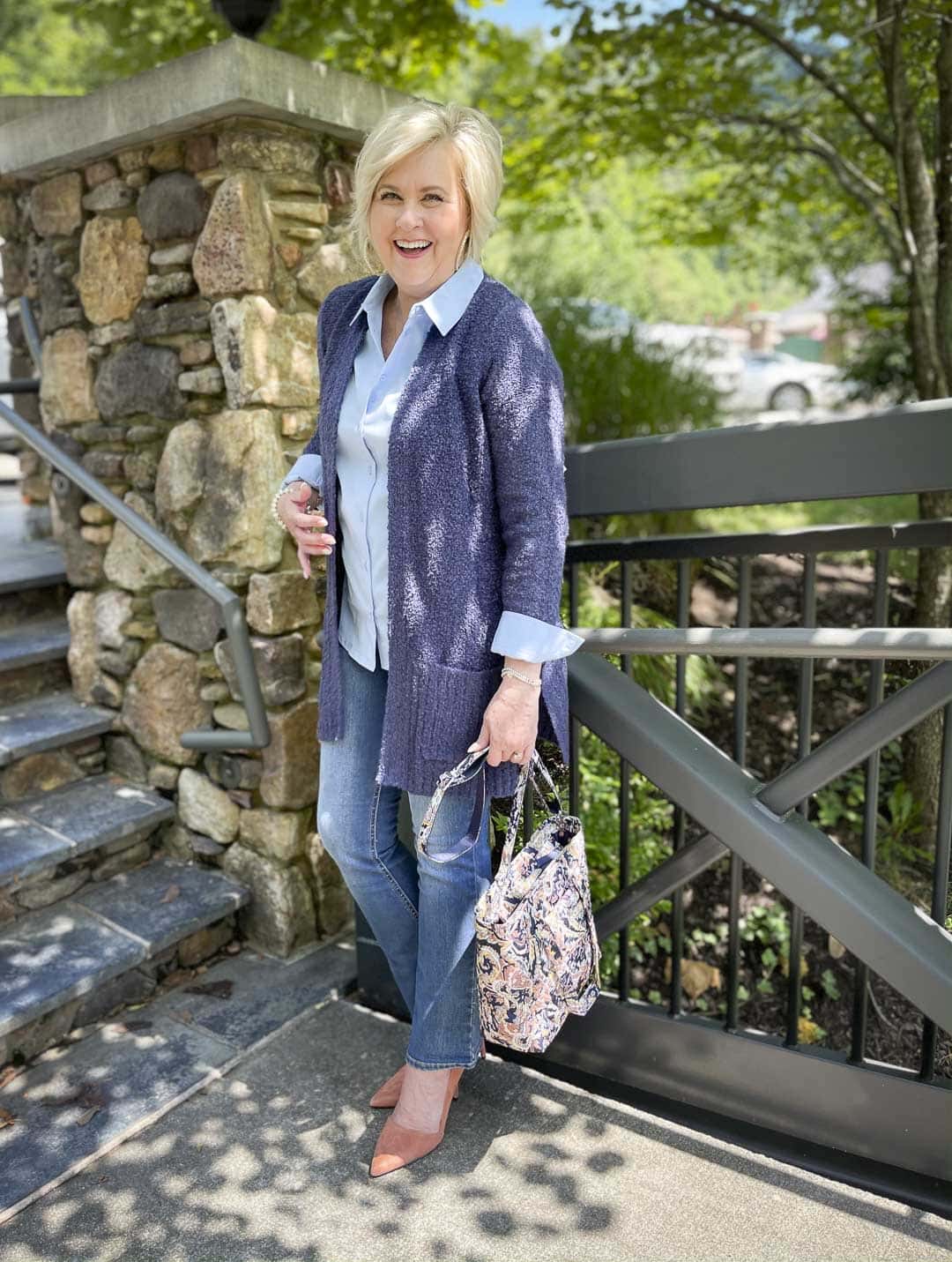 Over 40 Fashion Blogger, Tania Stephens is sitting on steps wearing a button shirt, a boucle cardigan, jeans, and holding her Vera Bradley handbag