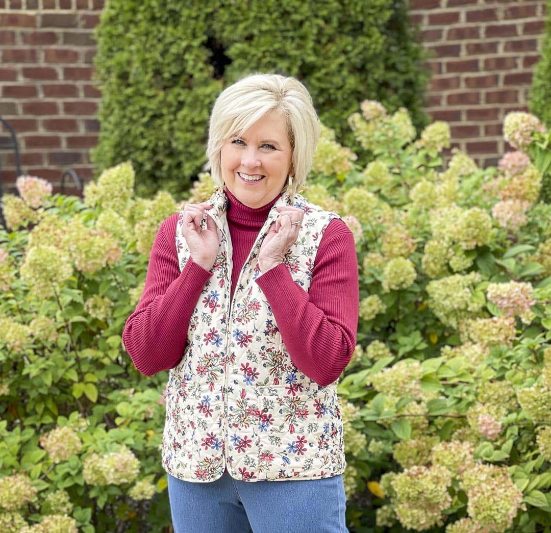 Over 40 fashion blogger, Tania Stephens, is wearing a vest in florals prints with a burgundy ribbed turtleneck that is perfect for fall