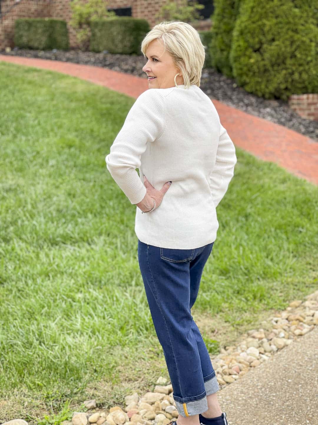 Over 40 Fashion Blogger, Tania Stephens is showing the back of a warm and cozy fall outfit of an ivory ribbed crewneck sweater, dark wash cuffed jeans, and navy Sperry sneakers