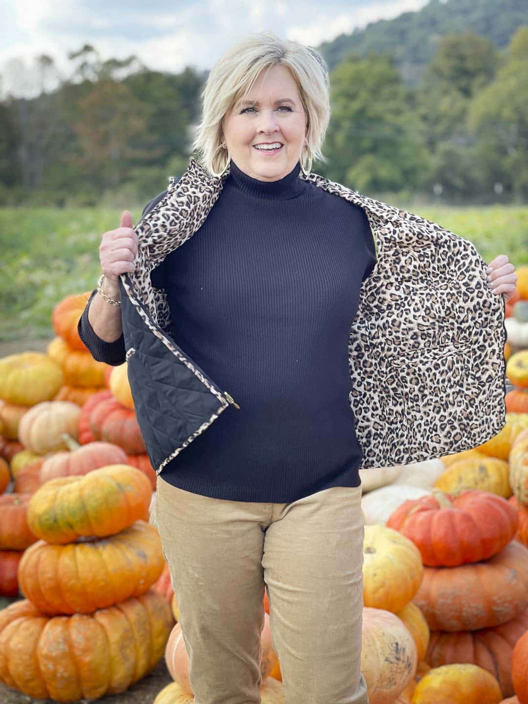 Over 40 Fashion Blogger, Tania Stephens, is in a pumpkin field wearing a reversible animal print vest with a black turtleneck from Appleseed's