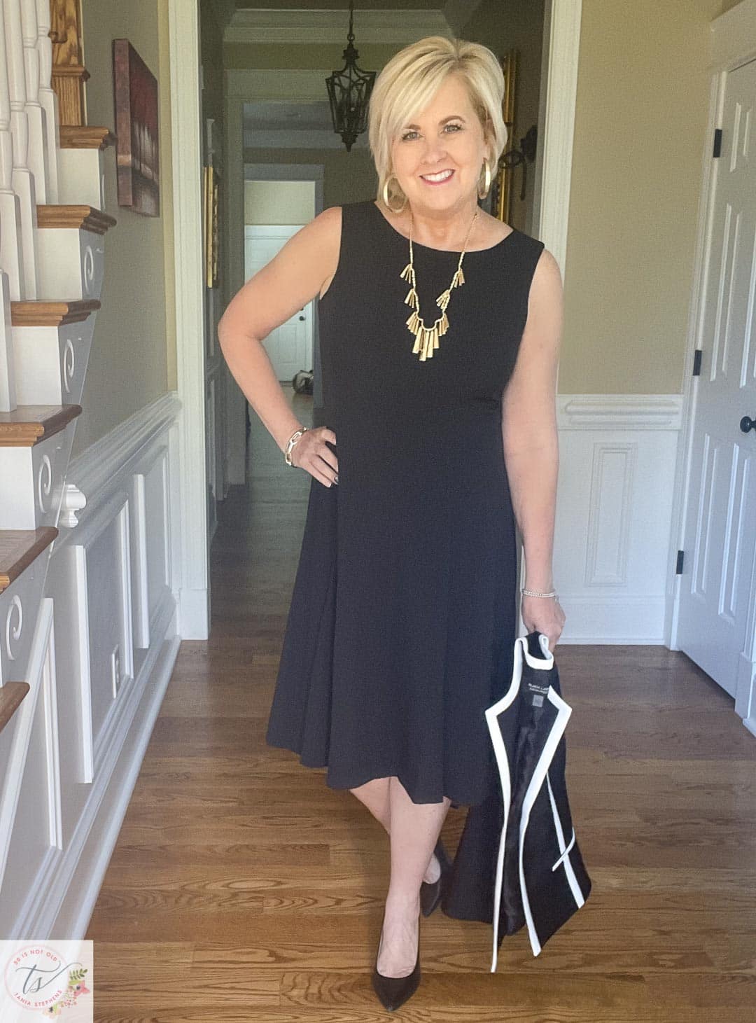 Over 40 Fashion Blogger, Tania Stephens is ready for a fall wedding wearing a black fit and flare dress and carrying a black and white jacket