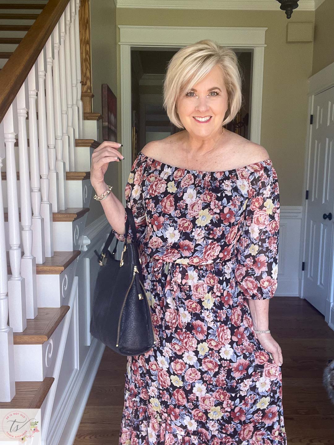 Over 40 Fashion Blogger, Tania Stephens is ready for a fall wedding wearing this off the shoulder floral print maxi dress with a black handbag