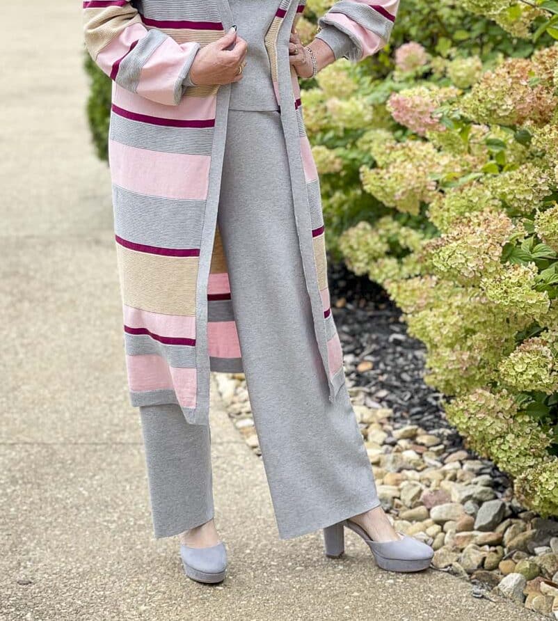 Over 40 fashion blogger, Tania Stephens, is standing by hydrangeas wearing a striped cardigan with a gray sweater tank and pants perfect for Thanksgiving Dinner