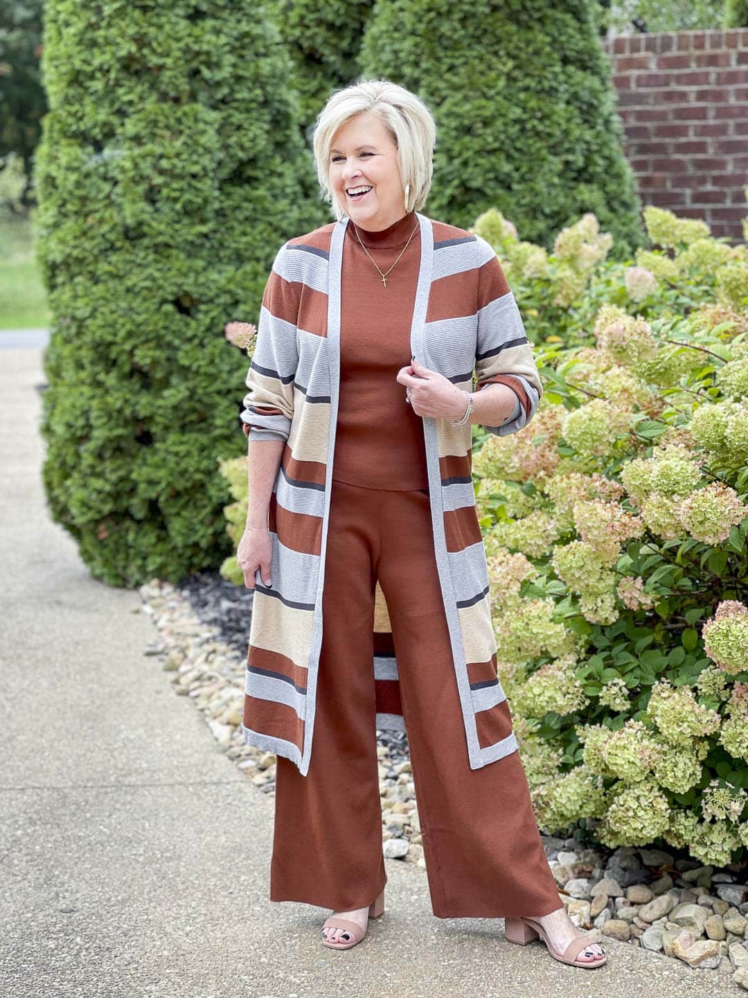 Over 40 fashion blogger, Tania Stephens, is laughing while wearing a striped cardigan with a dark rust sweater tank and pants perfect for Thanksgiving Dinner