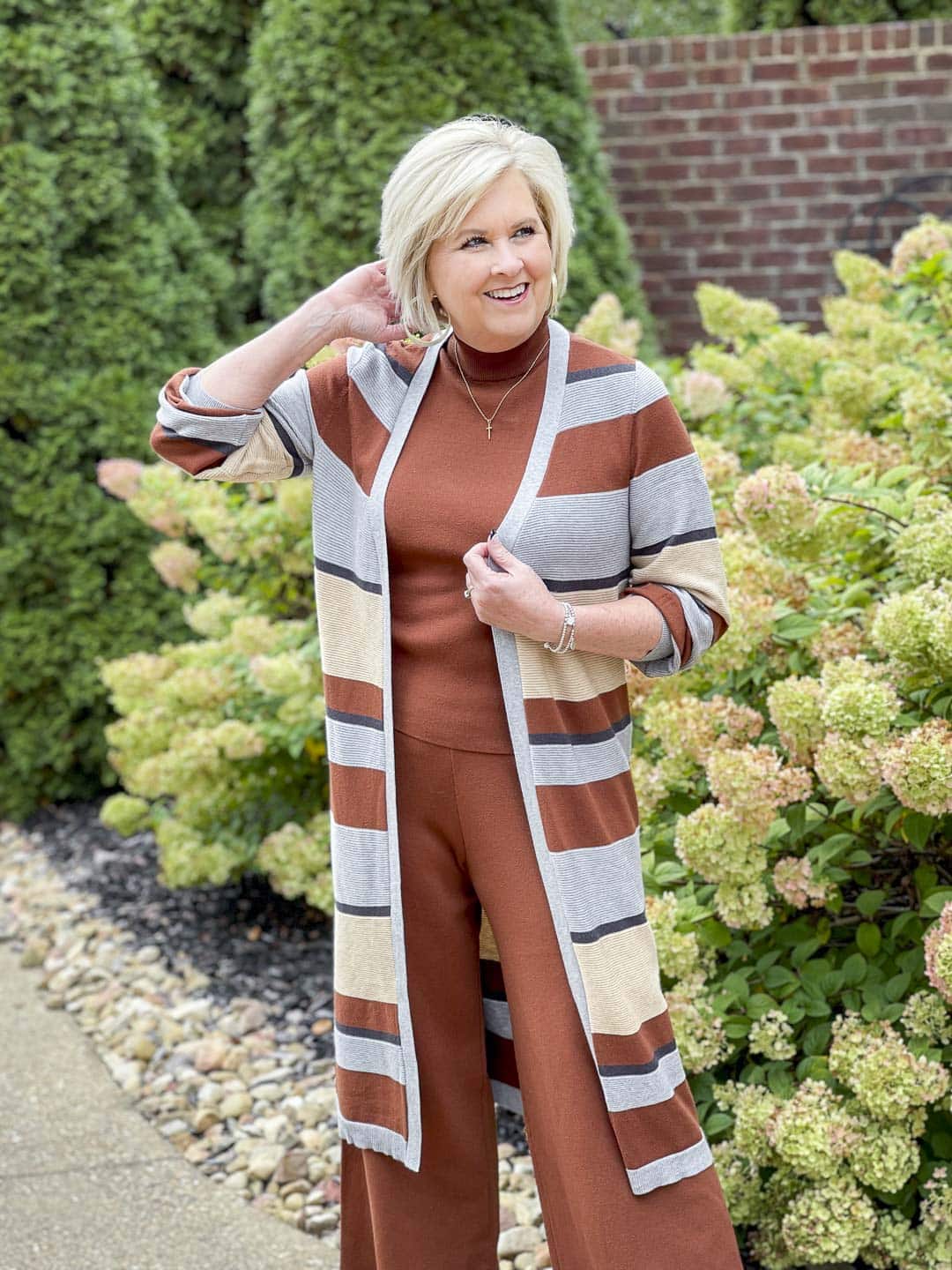 Over 40 fashion blogger, Tania Stephens, is wearing a striped cardigan with a dark rust sweater tank and pants with gold jewelry