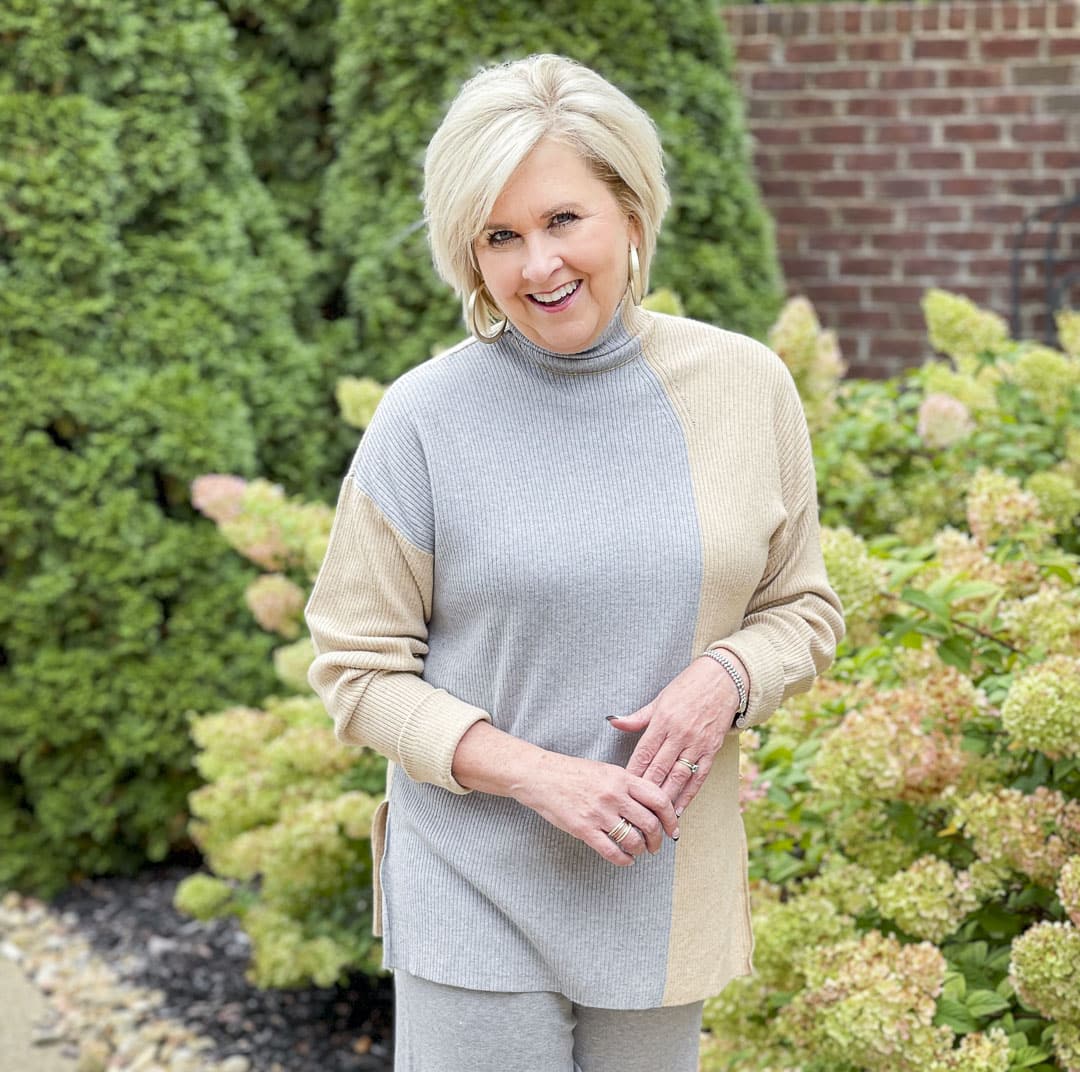 Over 40 fashion blogger, Tania Stephens, is standing by hydrangeas wearing a gray color block sweater