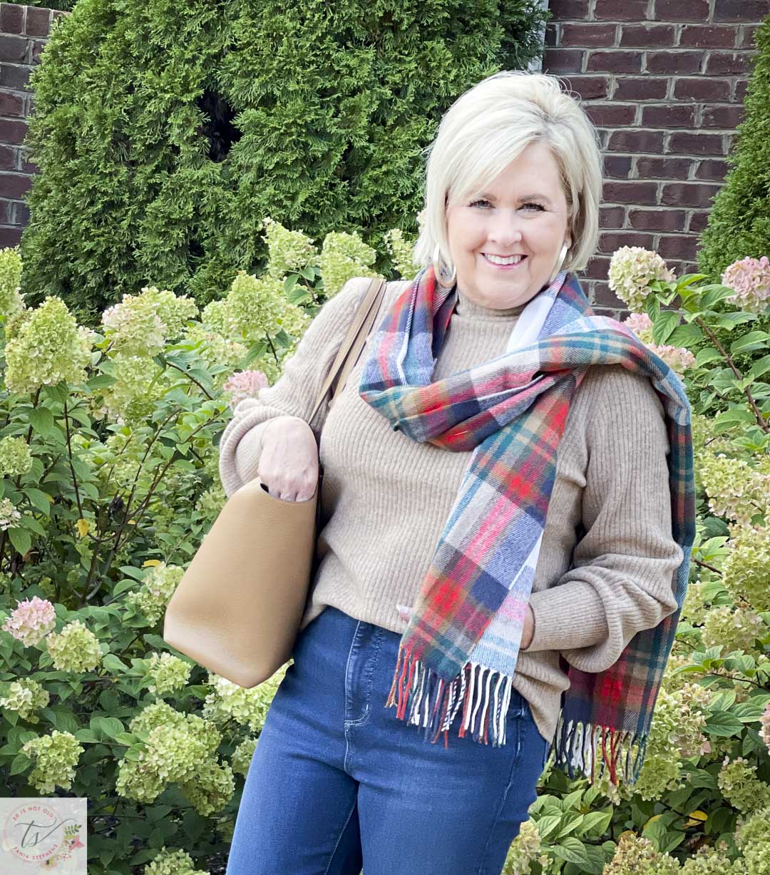 Over 40 Fashion Blogger, Tania Stephens, is wearing a ribbed mock neck sweater with a plaid scarf and is carrying a Tory Burch tote
