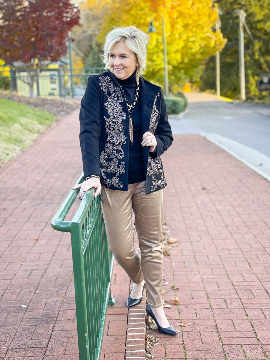 Over 40 Fashion Blogger, Tania Stephens is wearing a black turtleneck, a black and gold embellished jacket, gold ankle jeans, and black pumps