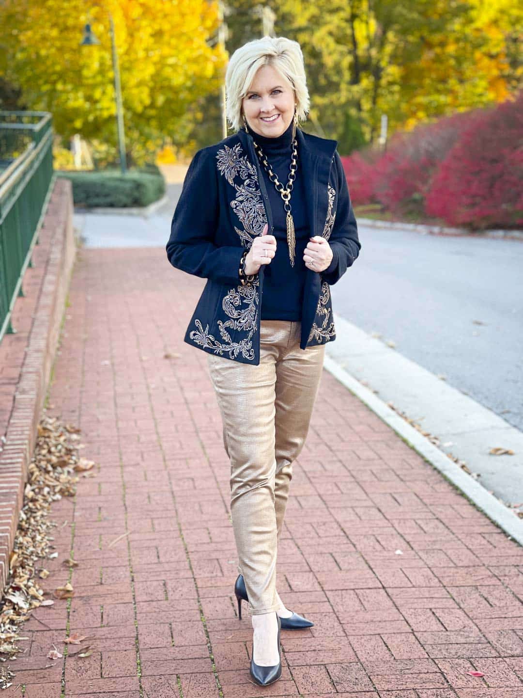 Over 40 Fashion Blogger, Tania Stephens is wearing a black turtleneck, a black and gold embellished jacket, gold ankle jeans, and black and gold jewelry