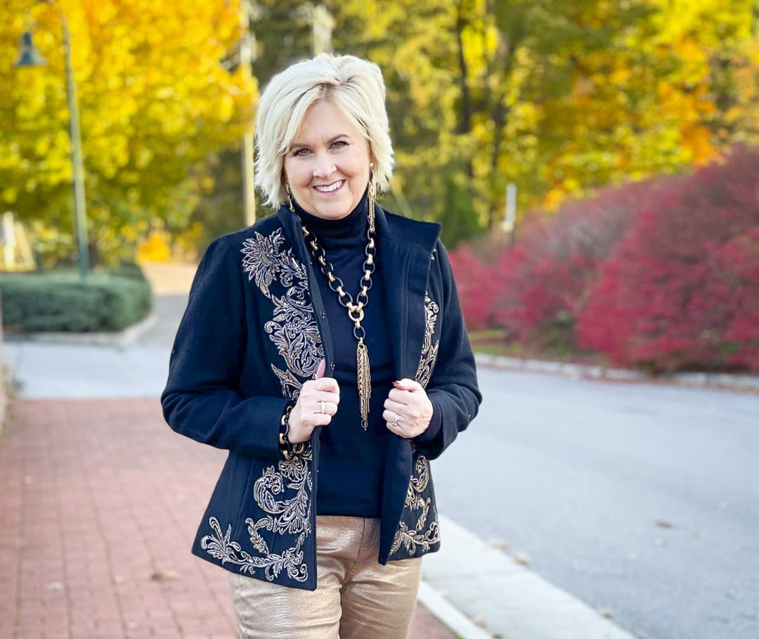 Over 40 Fashion Blogger, Tania Stephens is wearing a black turtleneck, a black embellished jacket, and black and gold jewelry