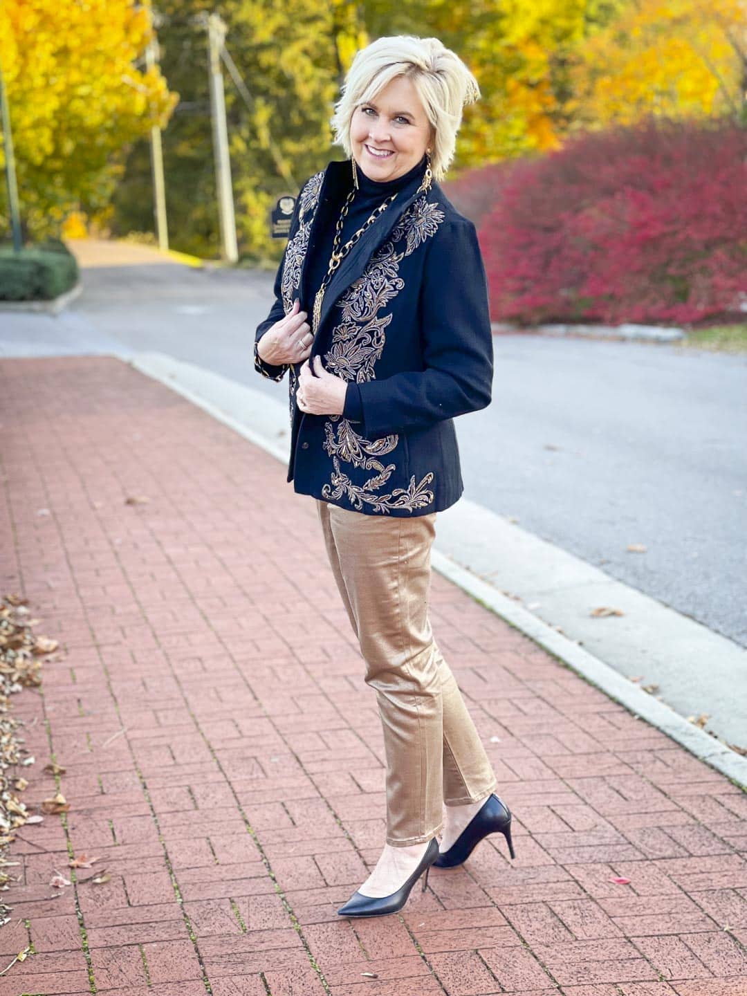 Over 40 Fashion Blogger, Tania Stephens is wearing a black turtleneck, a black and gold embellished jacket, gold ankle jeans, and black heels