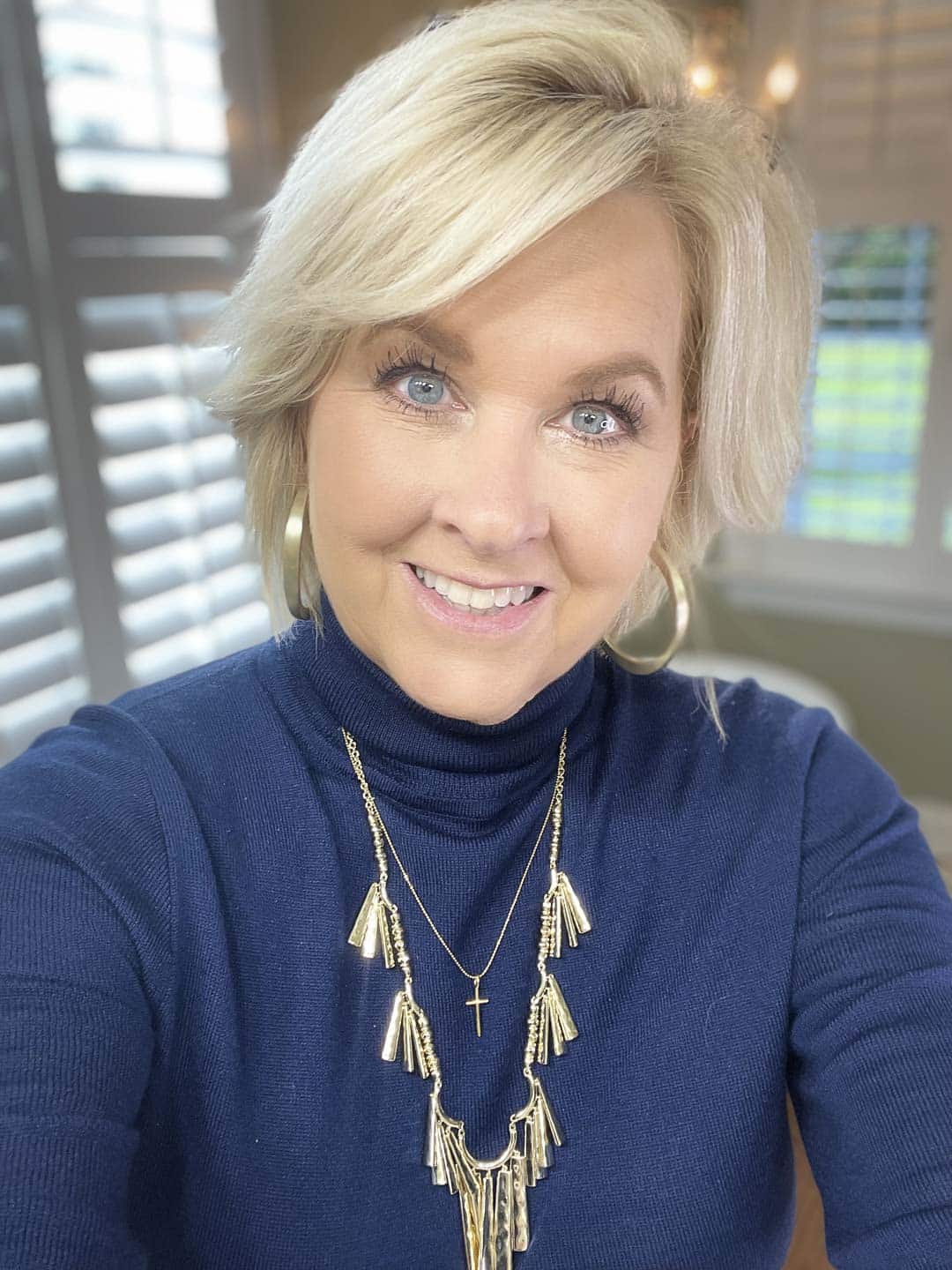 Over 40 Fashion Blogger, Tania Stephens is wearing a blue turtleneck and gold necklaces