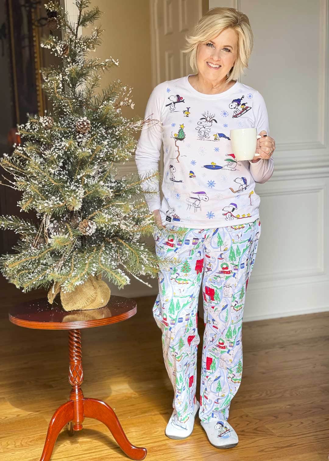 Over 40 Fashion Blogger, Tania Stephens is drinking her coffee while wearing A pair of Vera Bradley + Peanuts Ski Slope Snoopy pajamas and holding her dog, Lucy