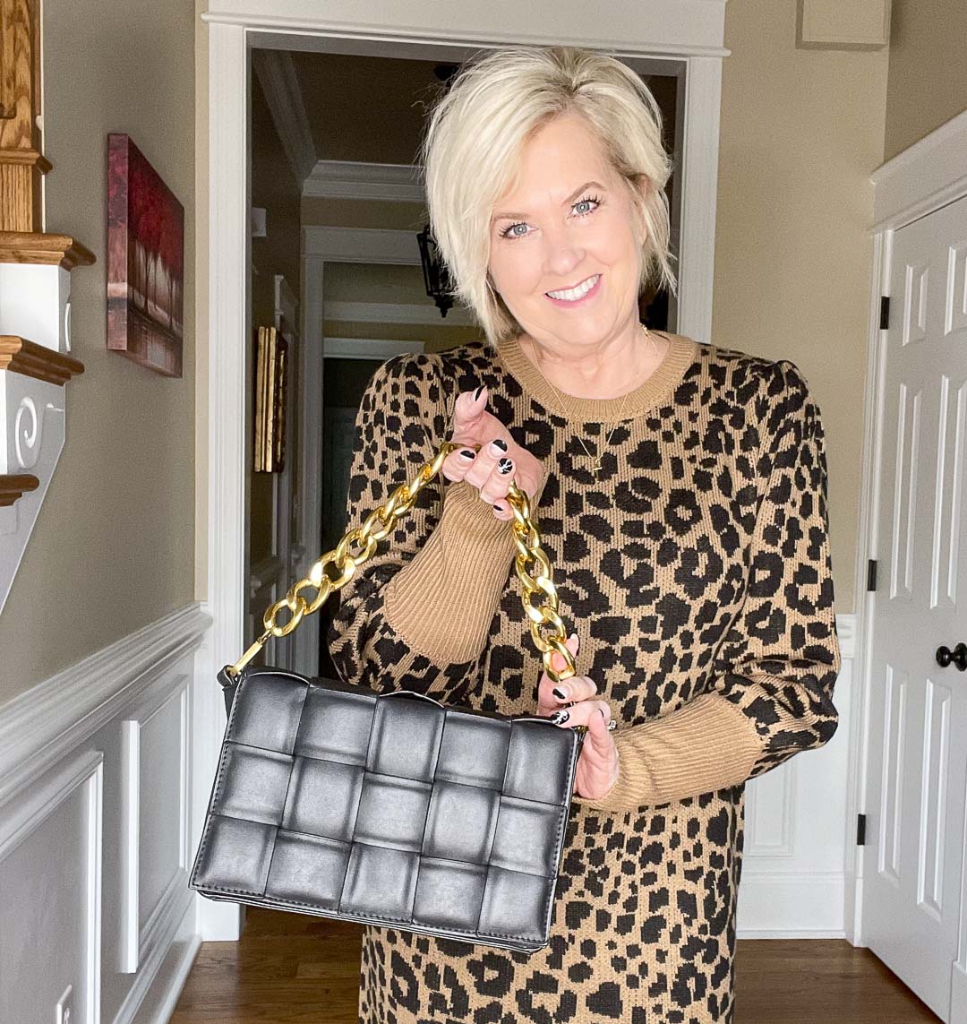 Over 40 Fashion Blogger, Tania Stephens is wearing a leopard print sweater dress and showing a black handbag