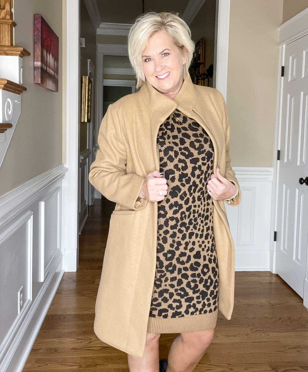 Over 40 Fashion Blogger, Tania Stephens is wearing a leopard print sweater dress, a camel faux-wool coat, and black ankle boots