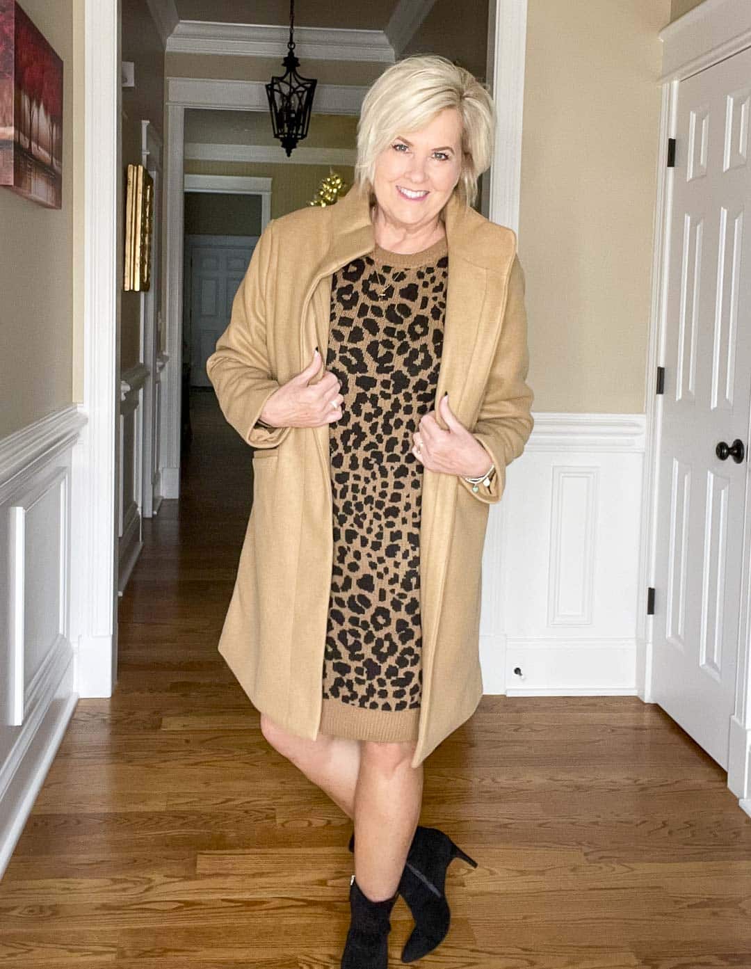 Over 40 Fashion Blogger, Tania Stephens is wearing a leopard-print sweater dress, a camel coat, and black ankle boots