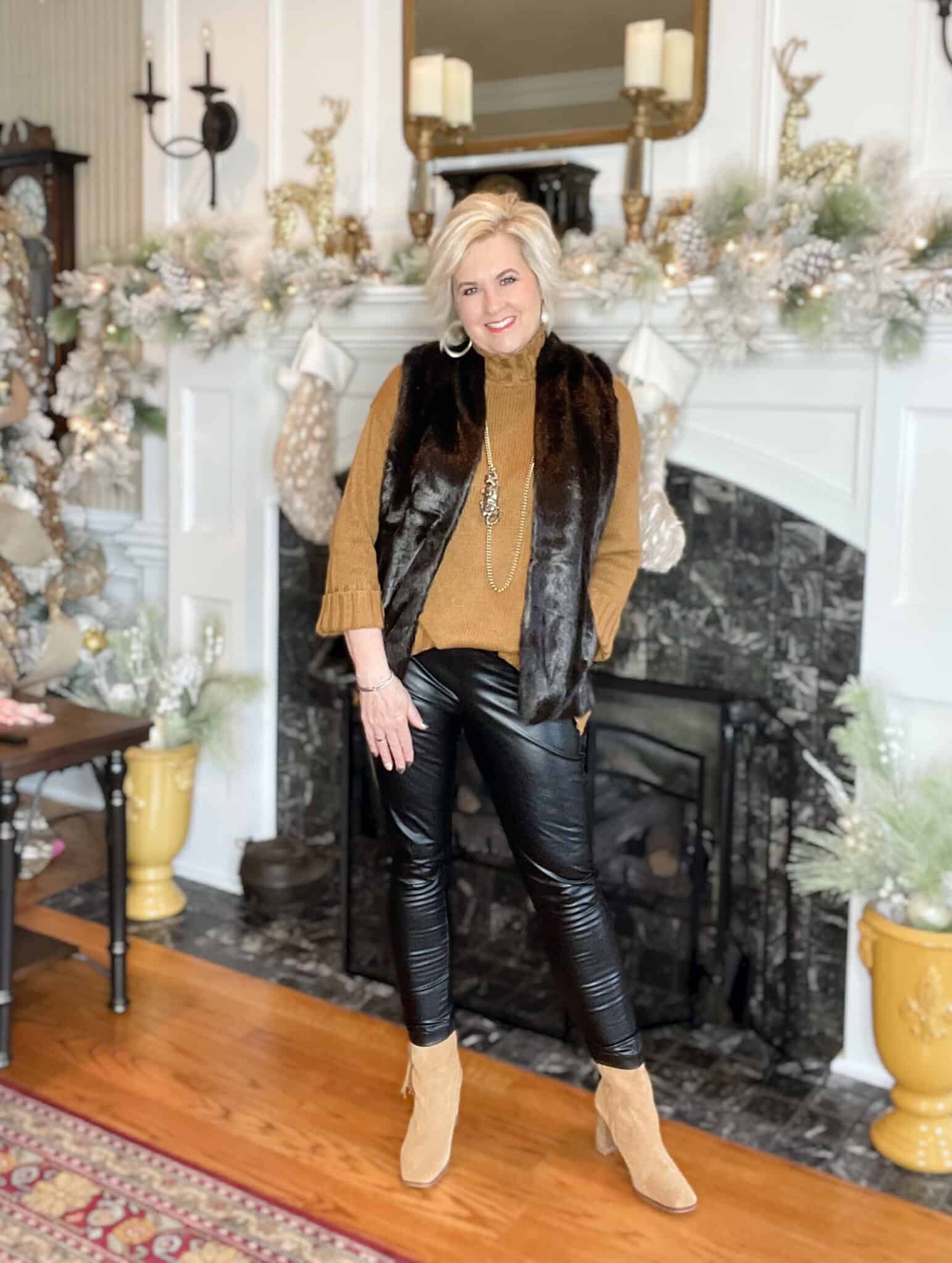 Over 40 Fashion Blogger, Tania Stephens is wearing a pair of faux leather leggings, a camel sweater, a faux fur vest, and fringe ankle boots
