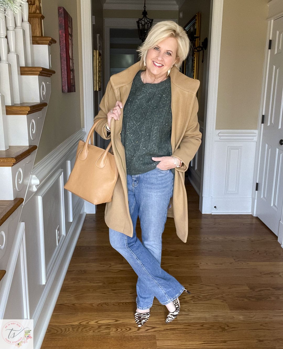 Over 40 Fashion Blogger, Tania Stephens is wearing a dark green sweater, jeans, animal heels, and a camel car coat