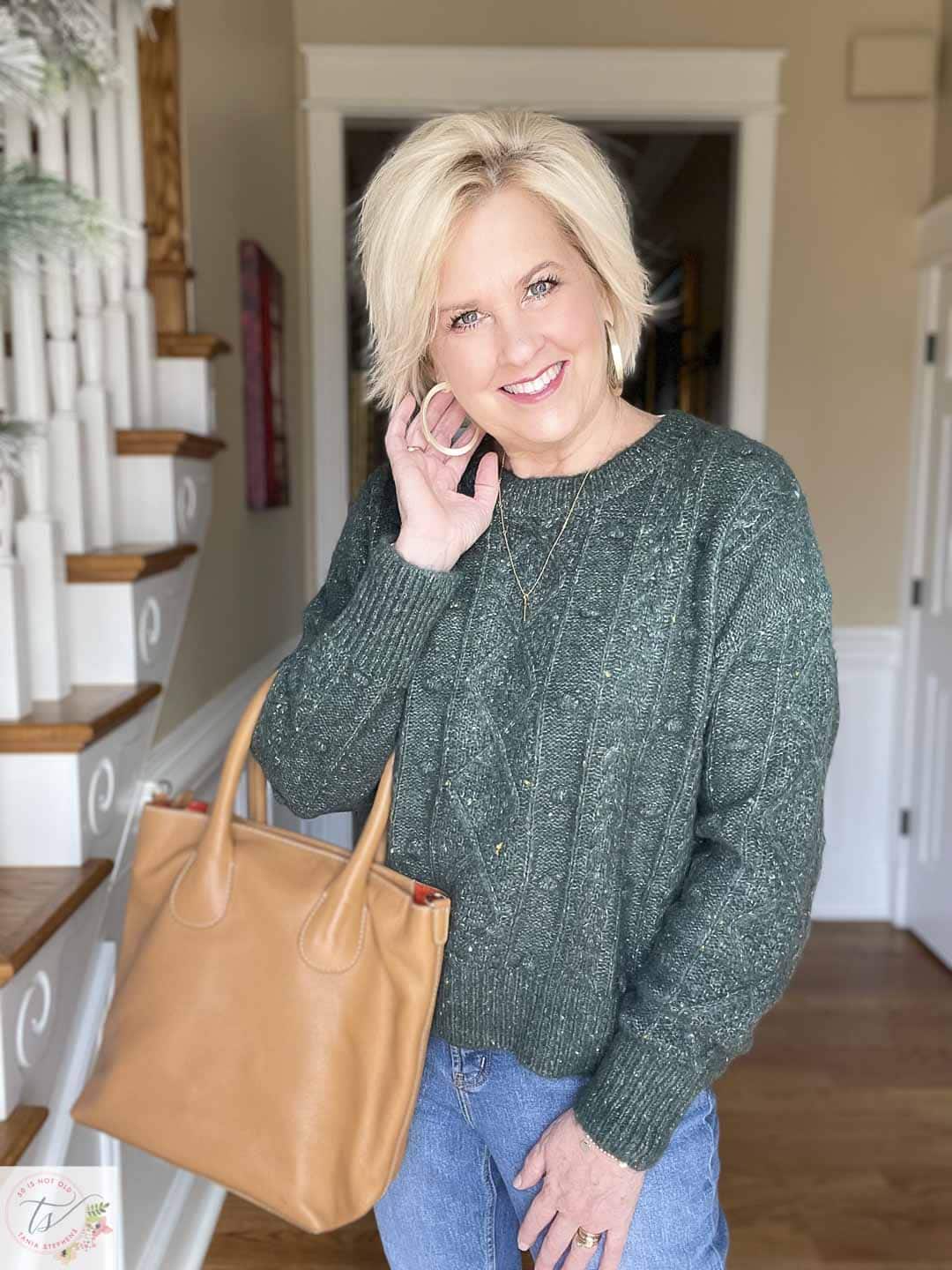 Over 40 Fashion Blogger, Tania Stephens is wearing a dark green sweater with gold hoop earrings