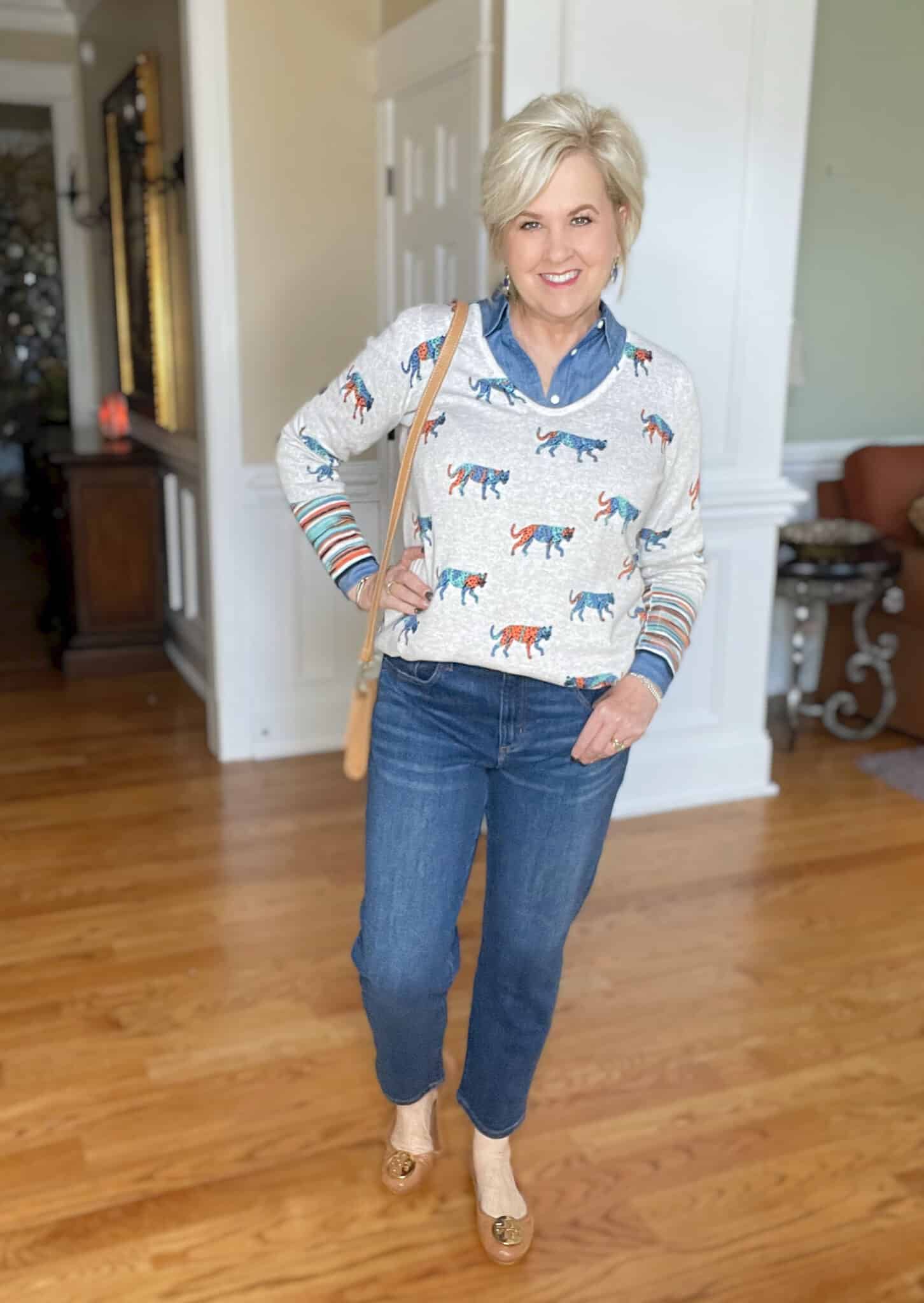 Over 40 Fashion Blogger, Tania Stephens is styling a chambray shirt under a bright leopard print sweater with tapered dark wash jeans and Tory Burch flats