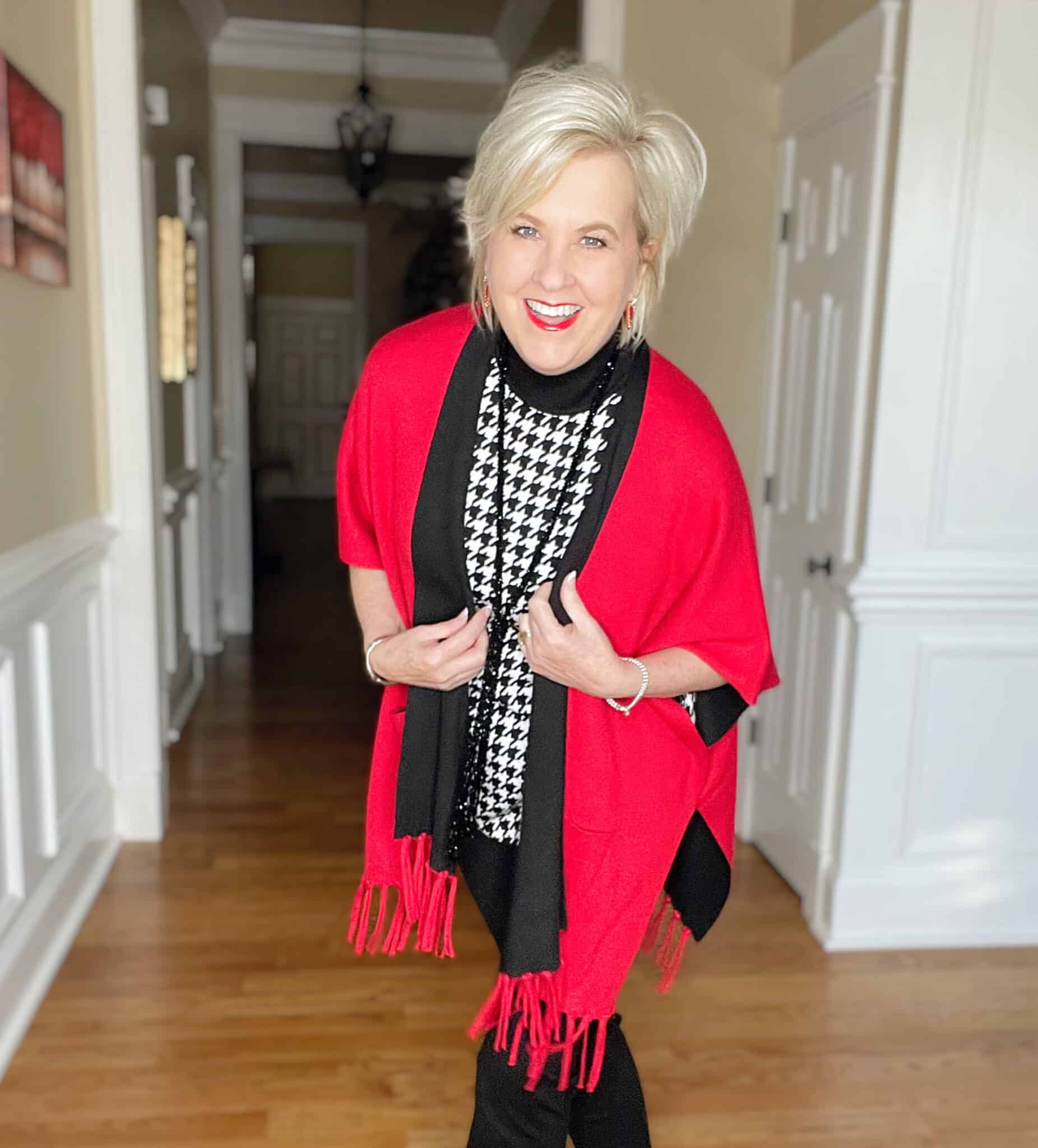 Over 40 Fashion Blogger, Tania Stephens is dressed in a herringbone print sweater, black pants, and a red-black reversible ruana