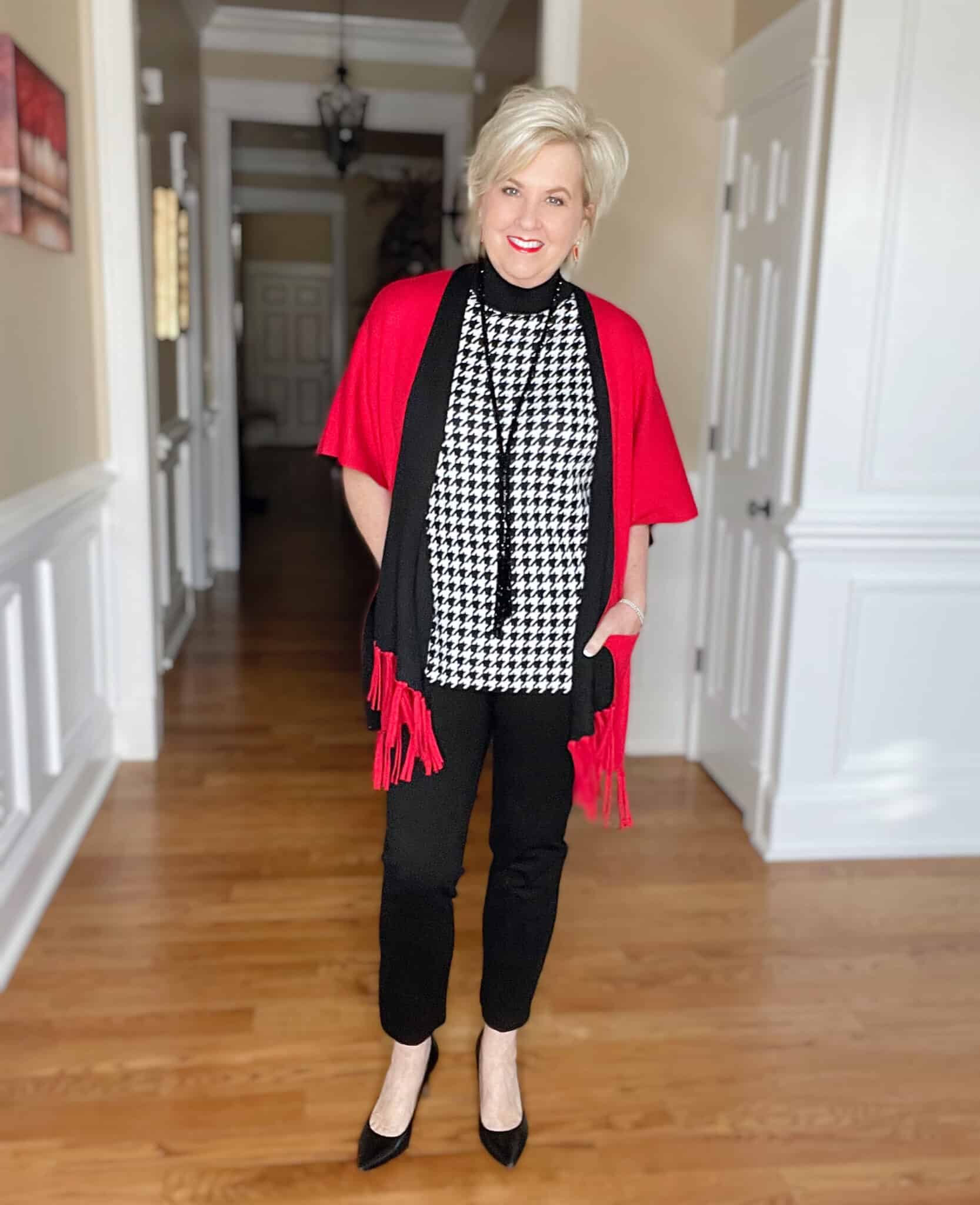 Over 40 Fashion Blogger, Tania Stephens is dressed in a herringbone print sweater, black pants, and a red/black reversible ruana from Chicos