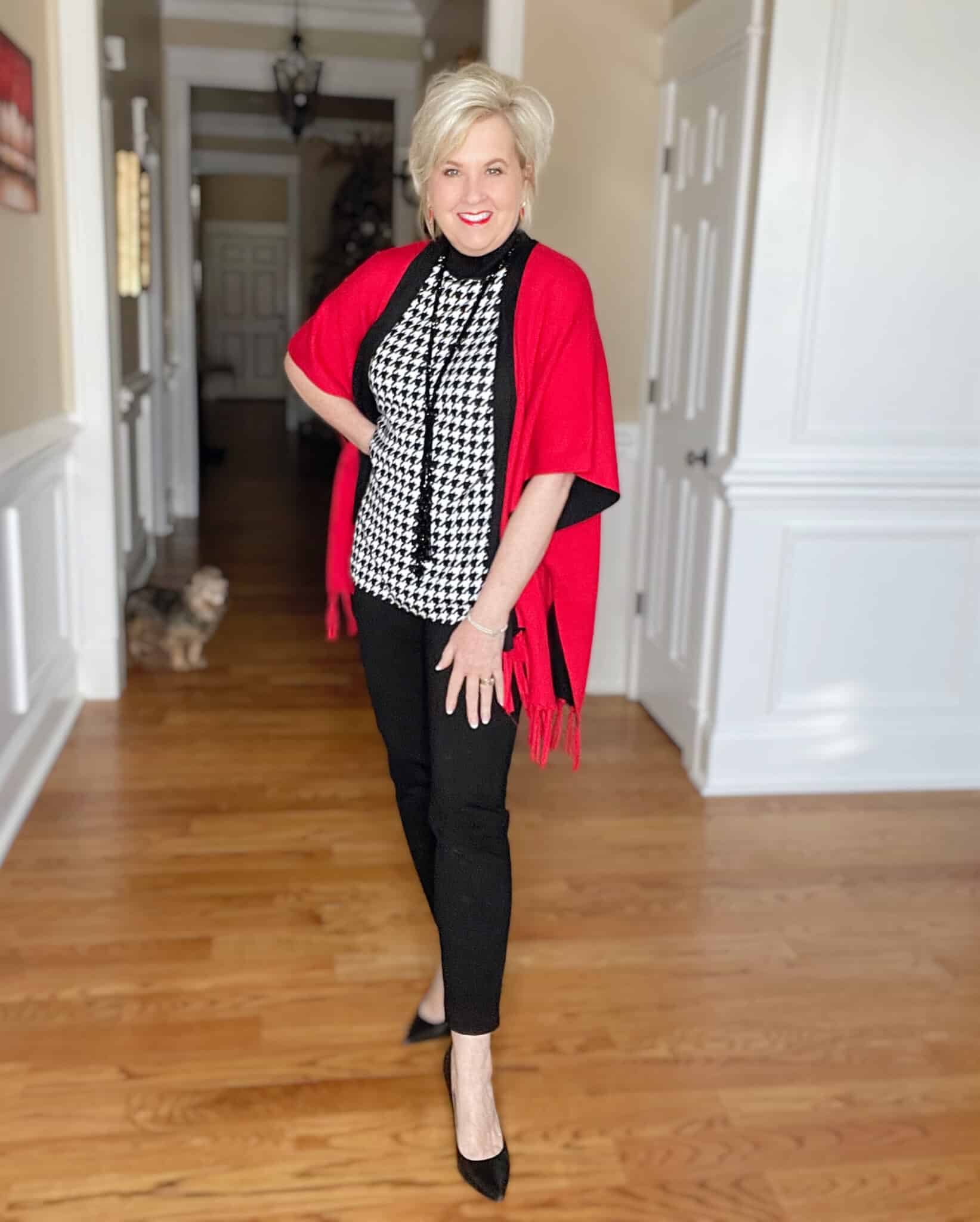 Over 40 Fashion Blogger, Tania Stephens is dressed in a herringbone print sweater, black pants, and a red/black reversible ruana