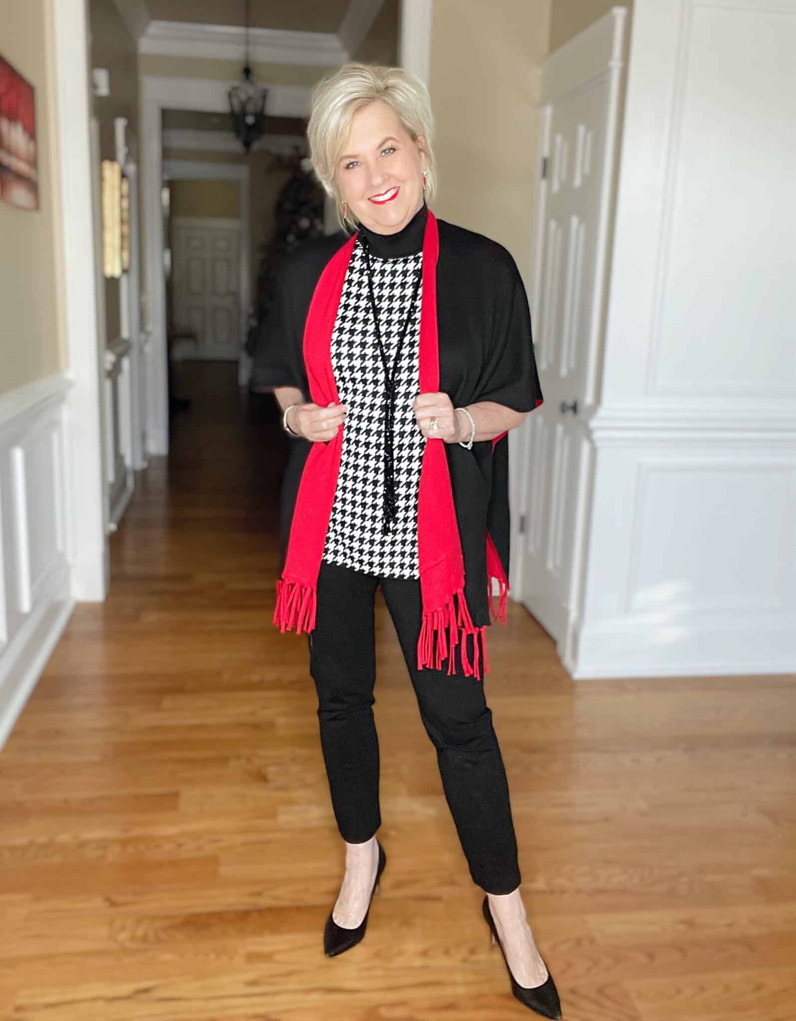 Over 40 Fashion Blogger, Tania Stephens is dressed in a herringbone print sweater, black pants, and a red/black reversible Ruana