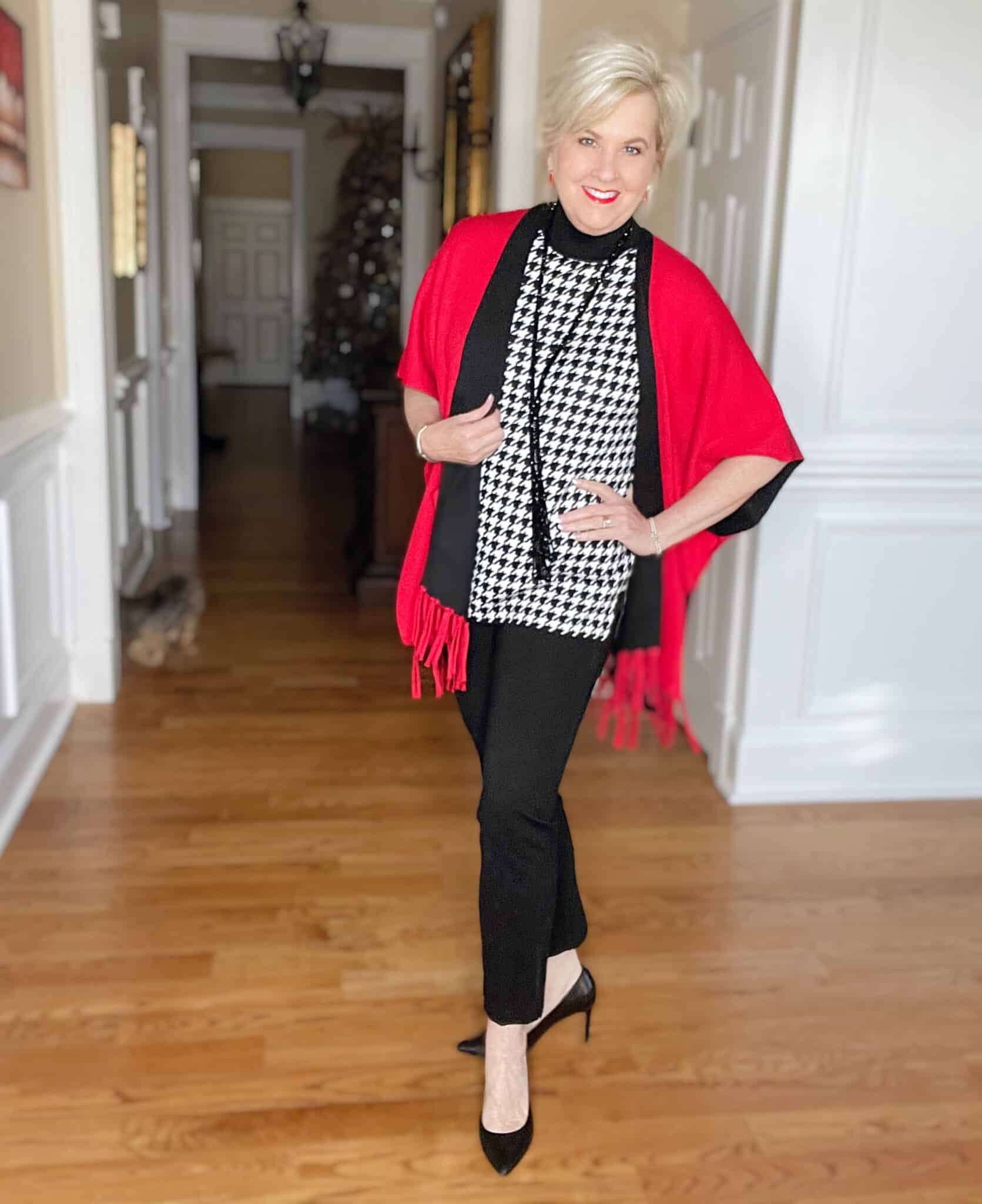 Over 40 Fashion Blogger, Tania Stephens is dressed in a herringbone print sweater, black pants, black pumps, and a red/black reversible ruana