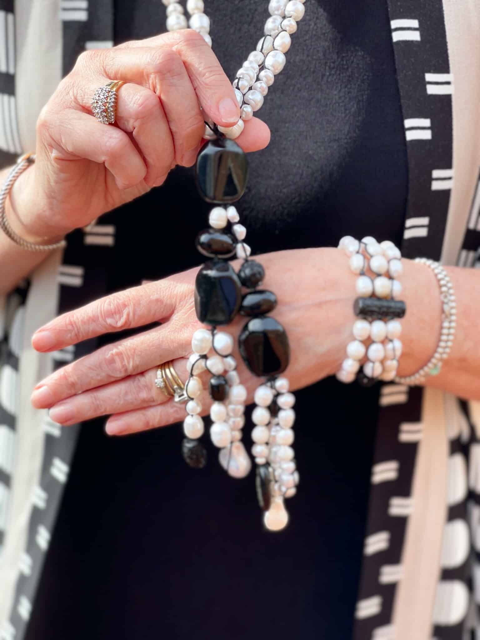 Over 40 Fashion Blogger, Tania Stephens is in front of a block wall wearing black and white jewelry