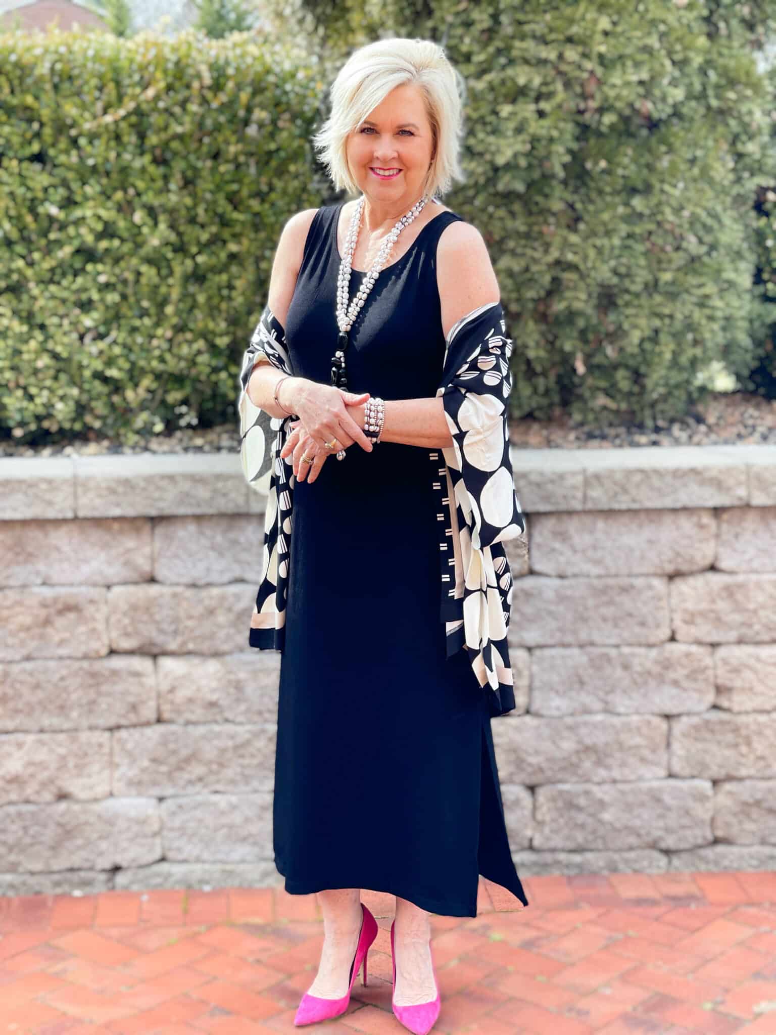 Over 40 Fashion Blogger, Tania Stephens is in front of a block wall wearing a black tank midi dress and a black and white ruana