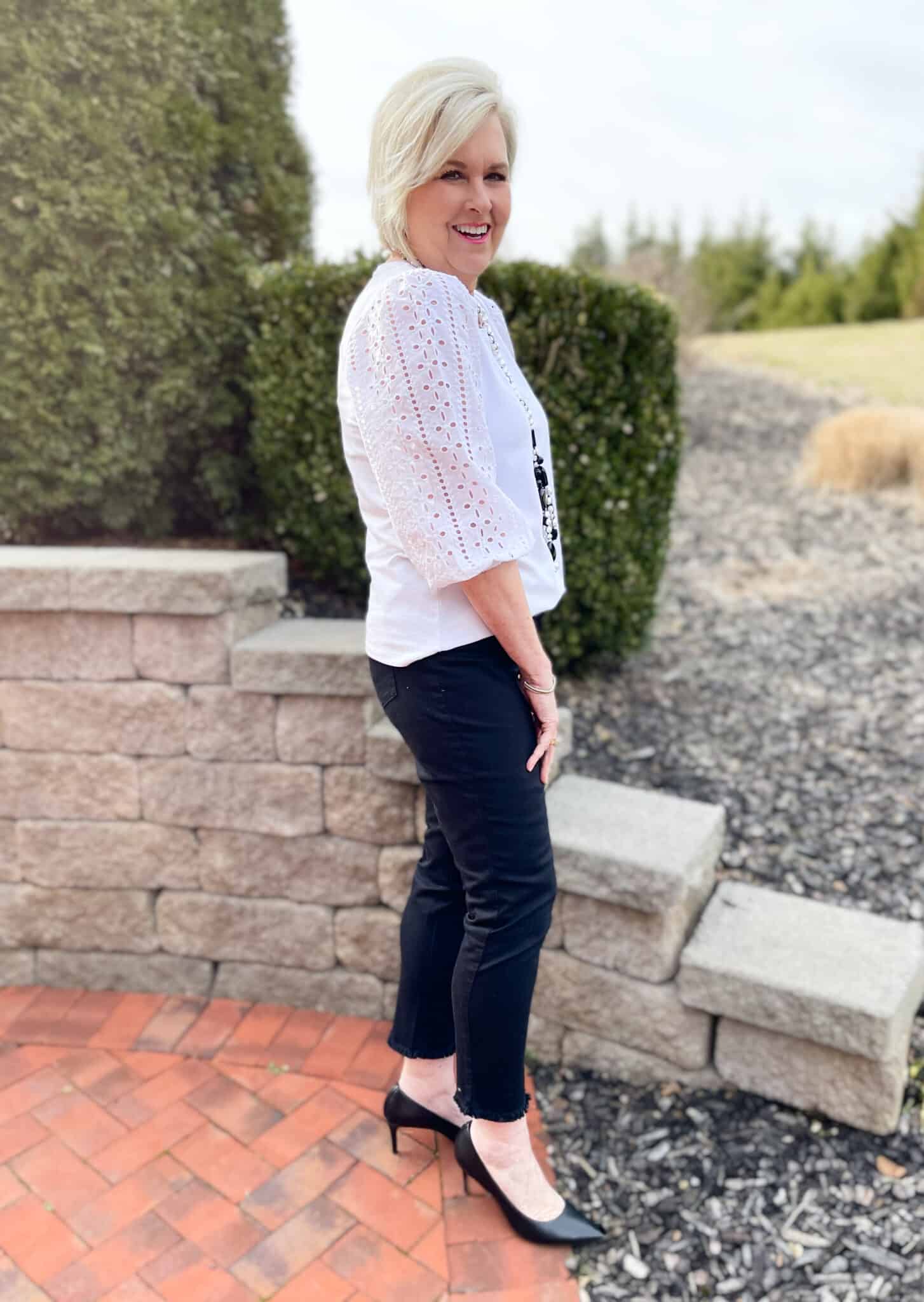 Over 40 Fashion Blogger, Tania Stephens is wearing a white eyelet top, black jeans, and black heels